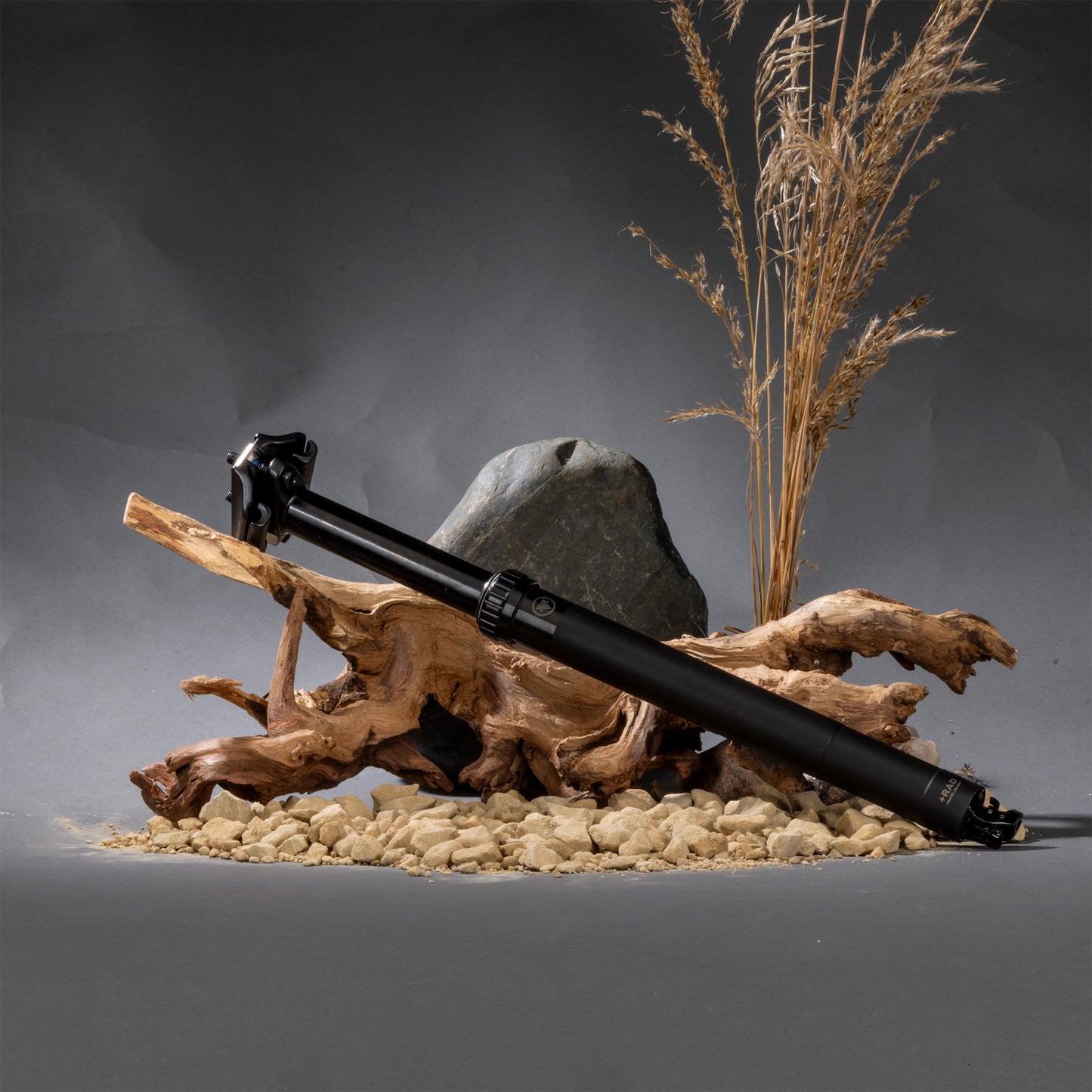 Black dropper seatpost on a gray surface with decorative elements like wood and plants.