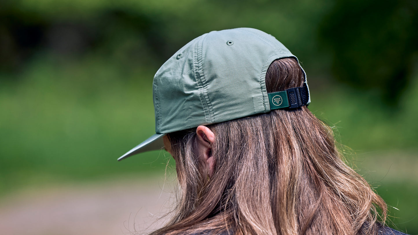 Person wearing green Teravail logo cap showing back detail with a blurred natural background