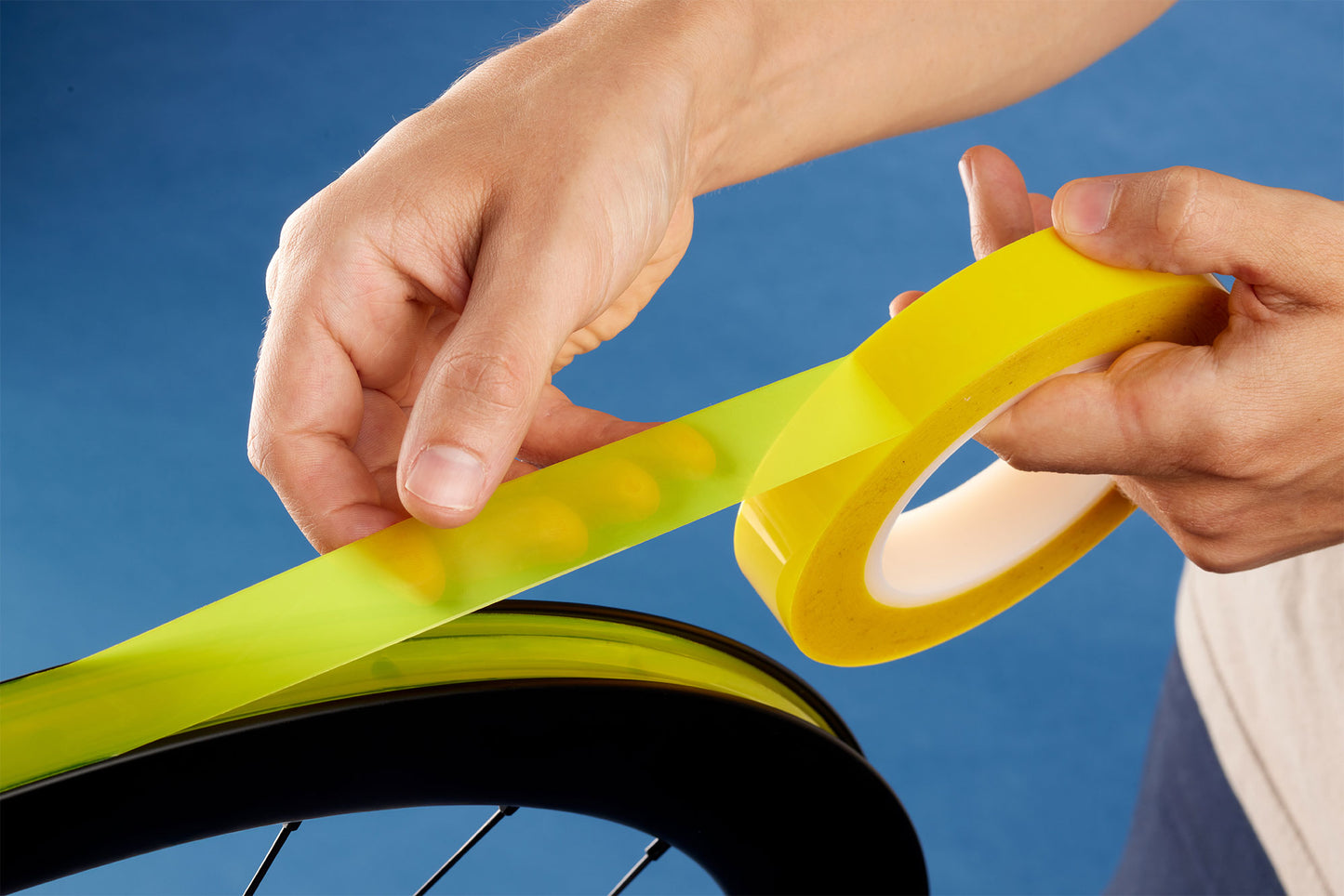 Person applying yellow tape to a bicycle rim against a blue background
