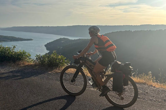 Hannah riding loaded mountain bike on mountain gravel road overlooking ocean and mountains
