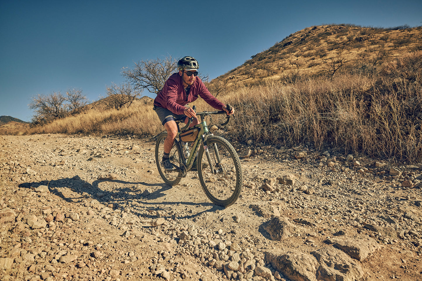 Person riding a bicycle on a rocky trail with a mountainous landscape in the background