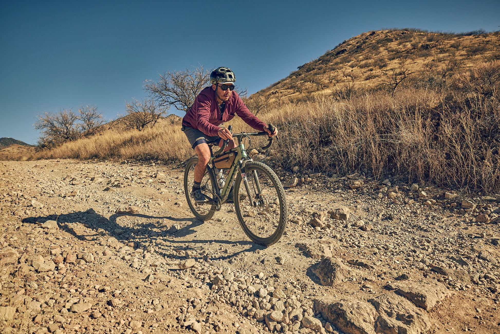Person riding a bicycle on a rocky trail with a mountainous landscape in the background