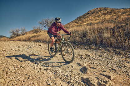 Person riding a bicycle on a rocky trail with a mountainous landscape in the background