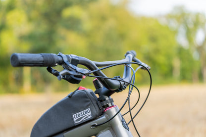 Close-up of a bicycle handlebar with Cedaero battery pack against a blurred natural background