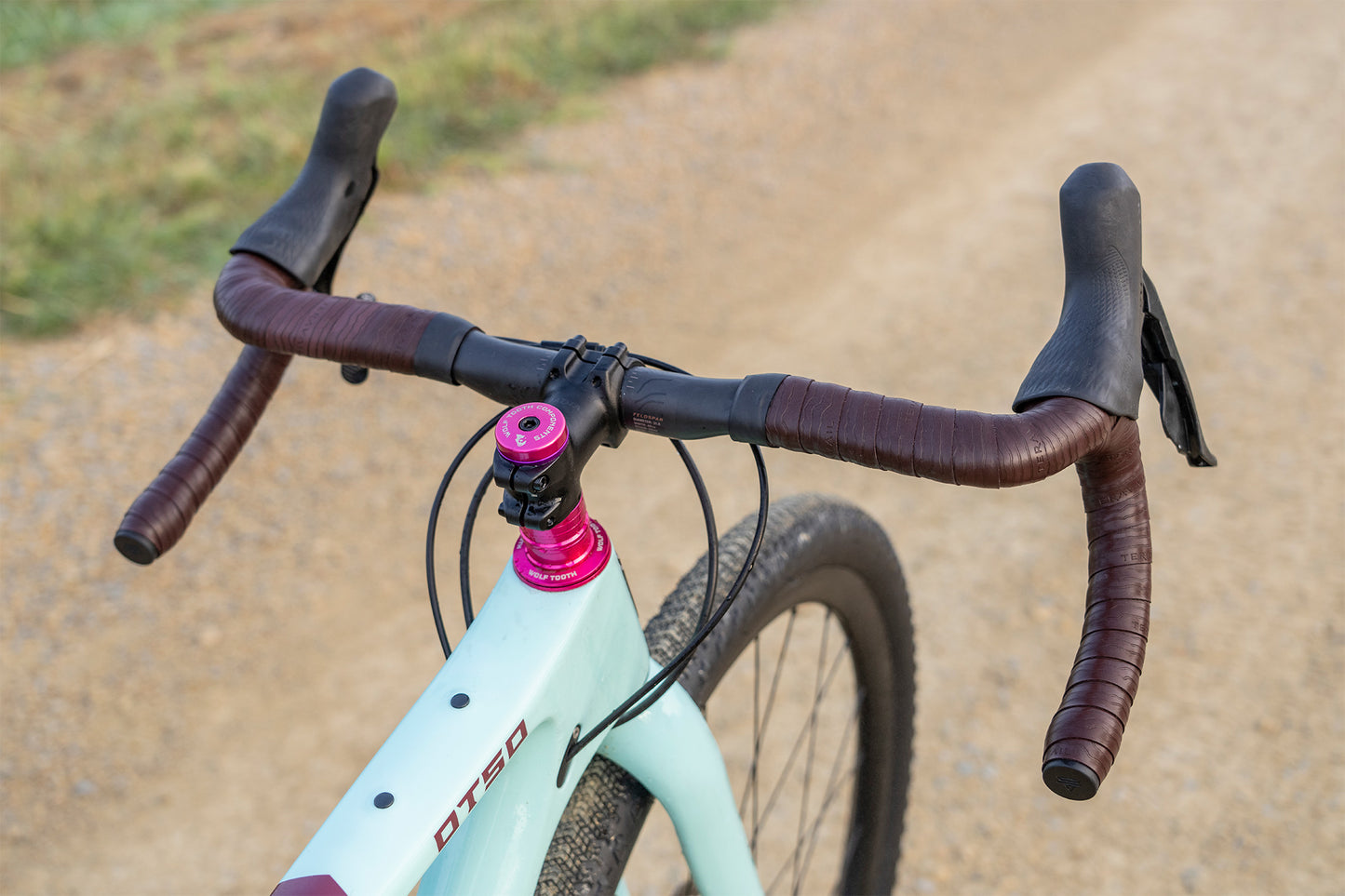 Close-up of a bicycle handlebar with a pink head tube on a dirt road