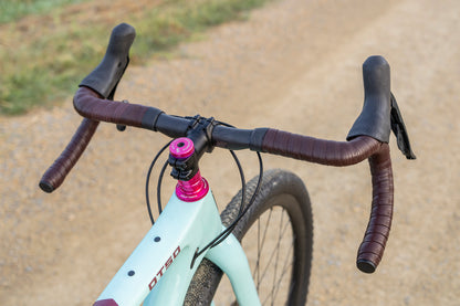 Close-up of a bicycle handlebar with a pink head tube on a dirt road