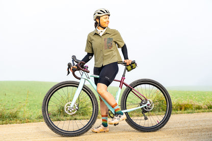 Person with a bicycle on a road with a green field in the background