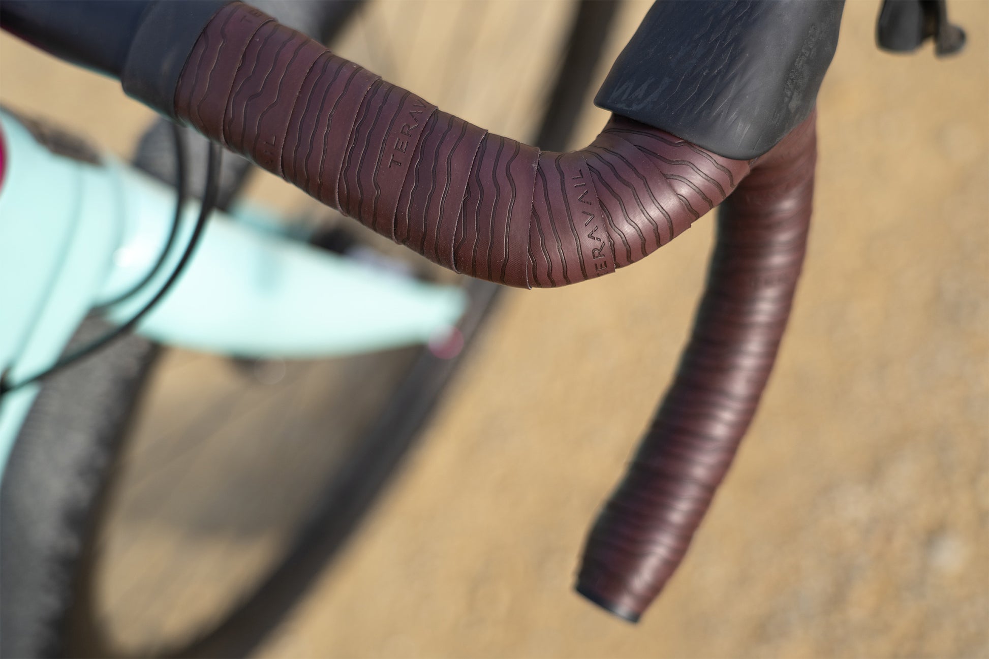 Close-up of dark red Teravail Radia bar tape on bike with blurry gravel background