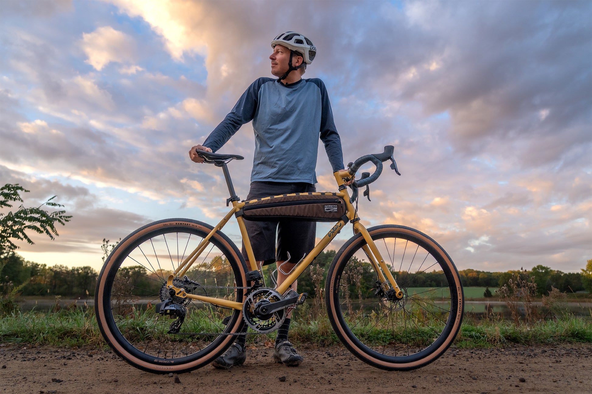 Man with a bicycle standing on a dirt path with a cloudy sky background