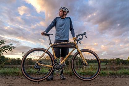 Man with a bicycle standing on a dirt path with a cloudy sky background
