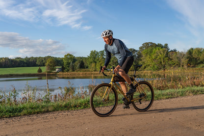Person riding a bicycle on a dirt path near a lake with trees in the background
