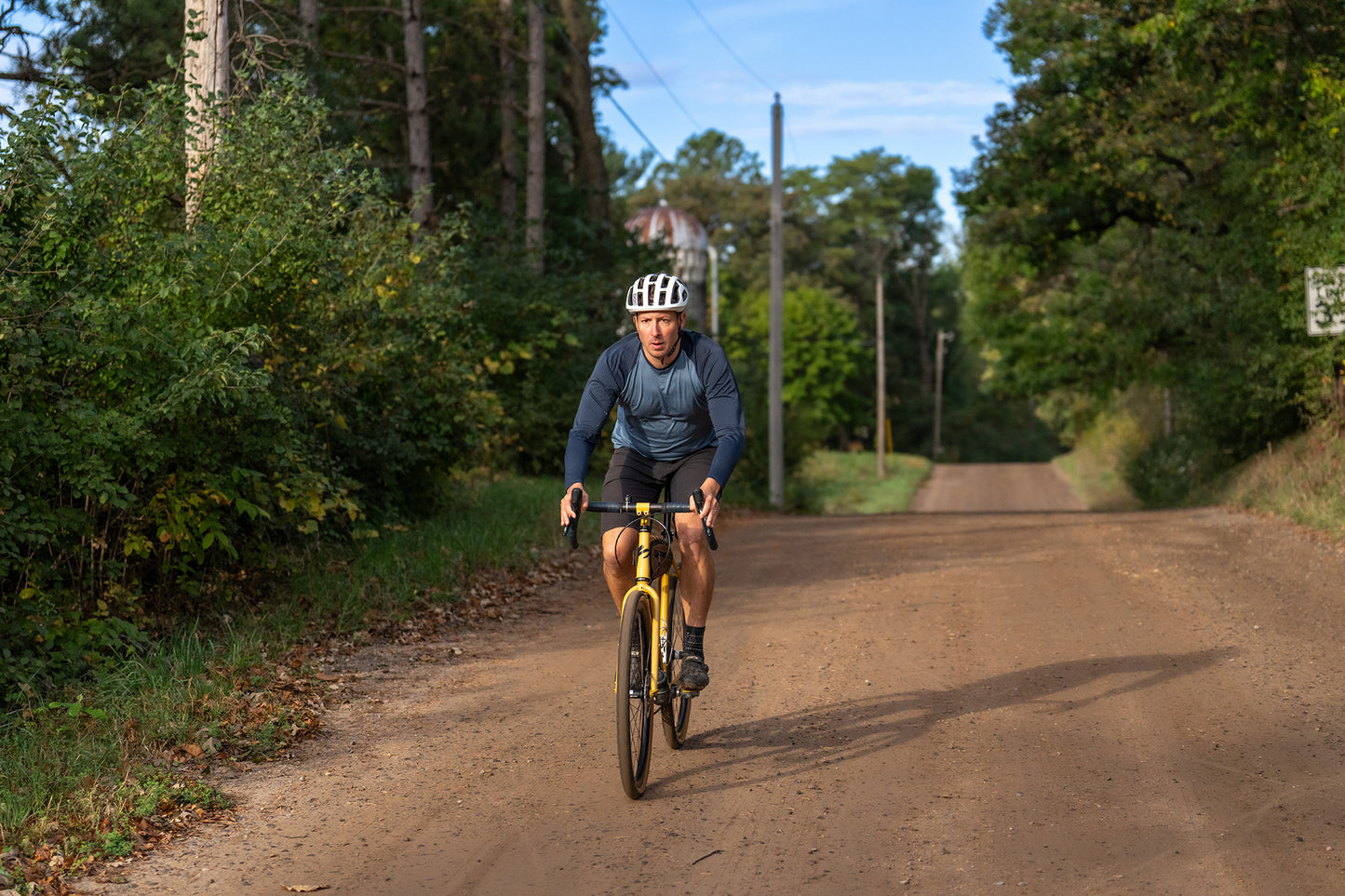 Person riding a bicycle on a dirt road surrounded by trees