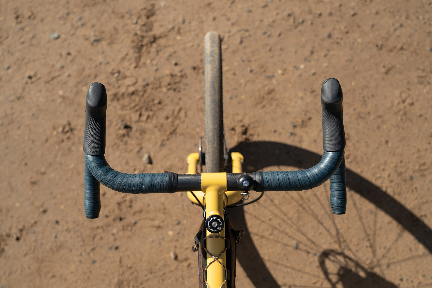 Bicycle handlebar with black grips and yellow frame on a brown dirt background