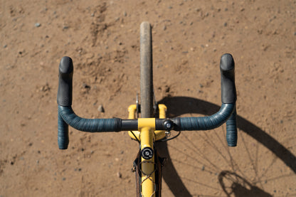 Bicycle handlebar with black grips and yellow frame on a brown dirt background