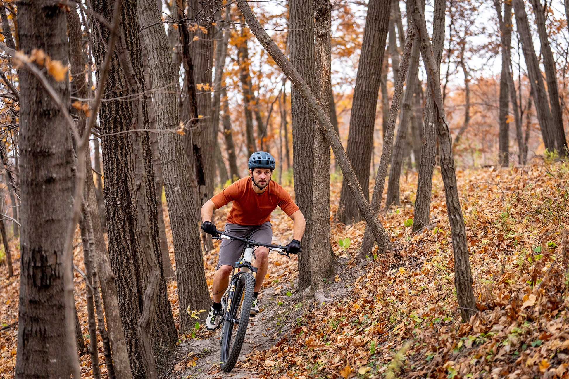 Man riding a mountain bike through a forest with autumn leaves
