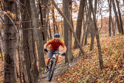 Man riding a mountain bike through a forest with autumn leaves