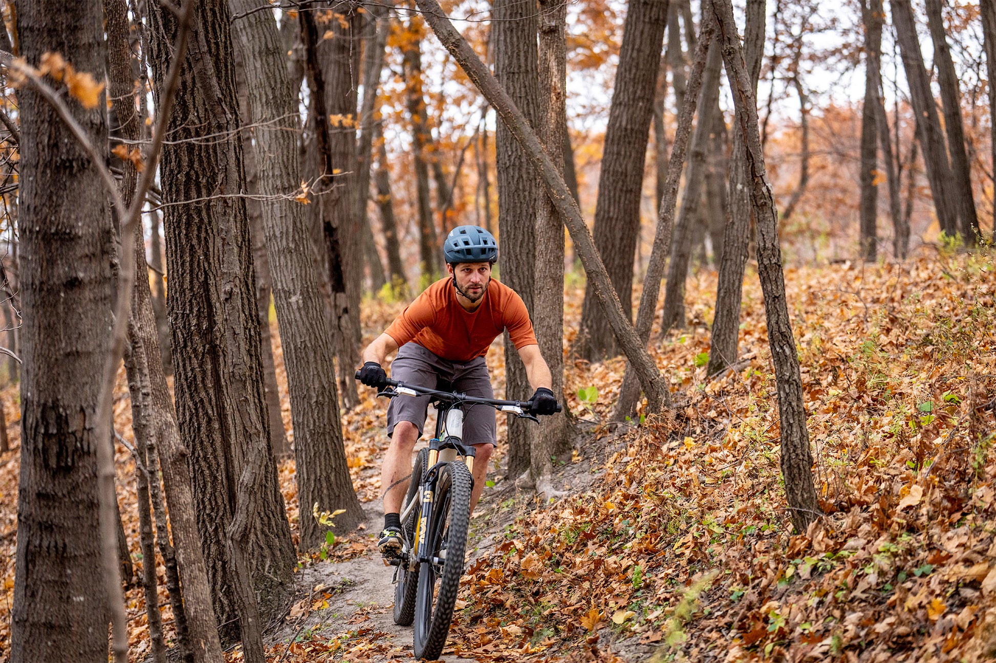 Person riding a mountain bike through a forest with autumn leaves