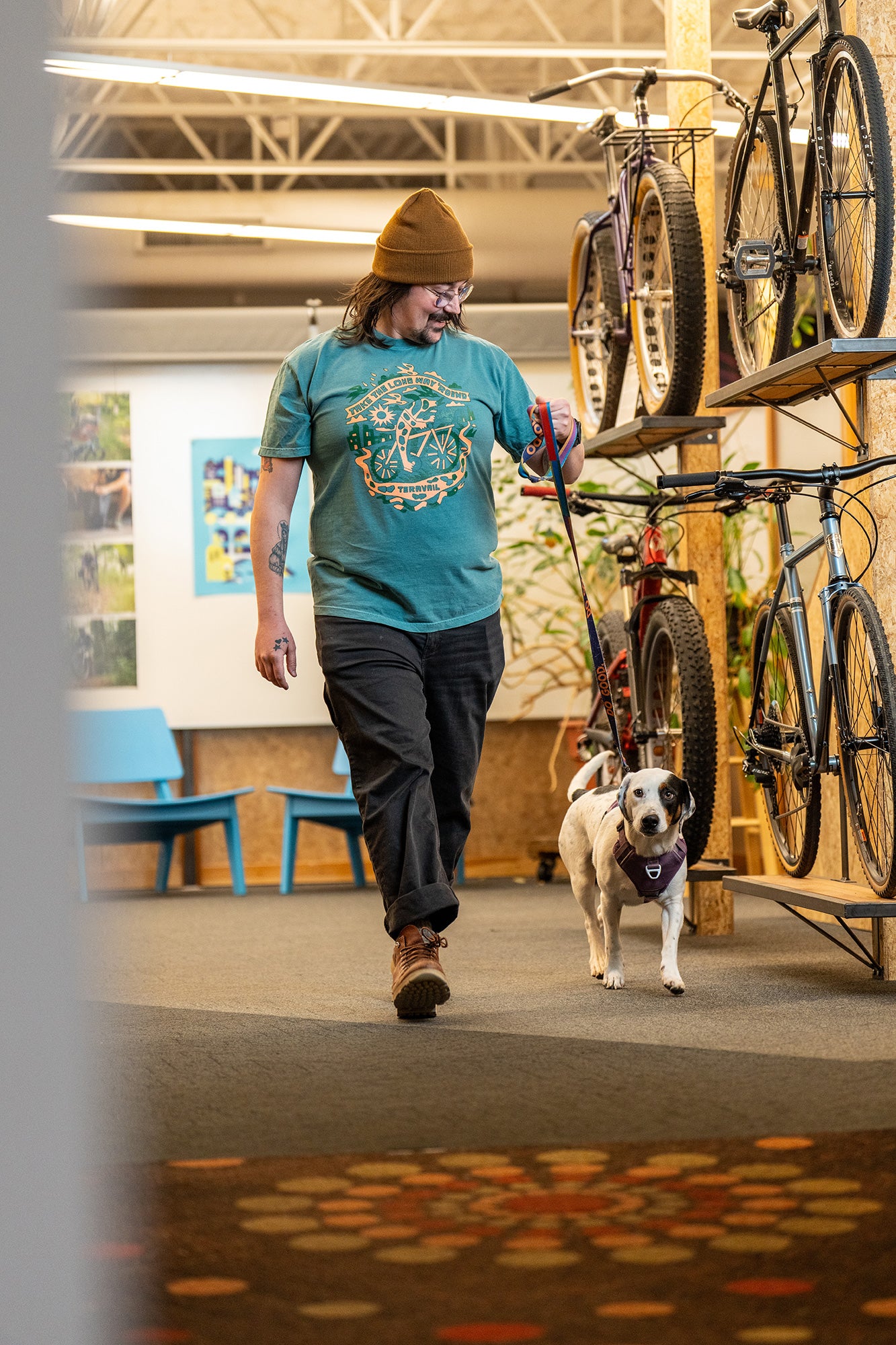 Man walking a dog in a room with bicycles and colorful floor.