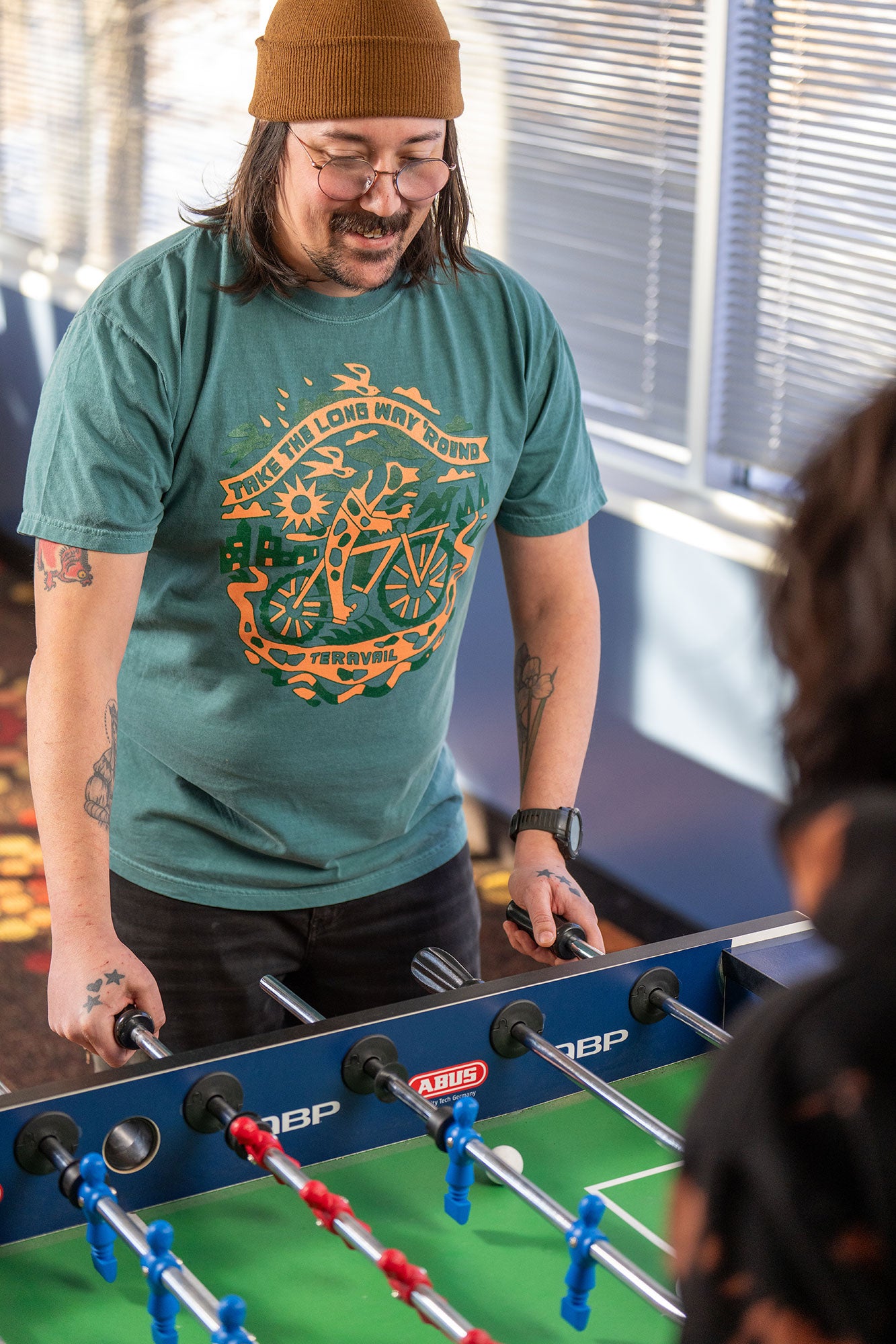 Man playing foosball wearing a green t-shirt with a graphic design.