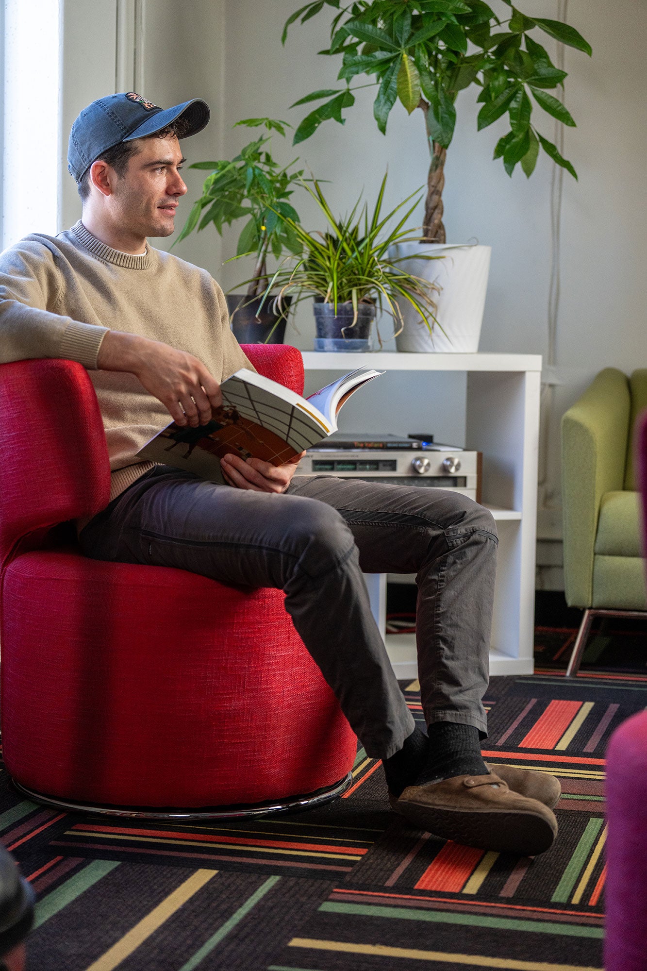 Man sitting on a red chair reading a book in a cozy living room.