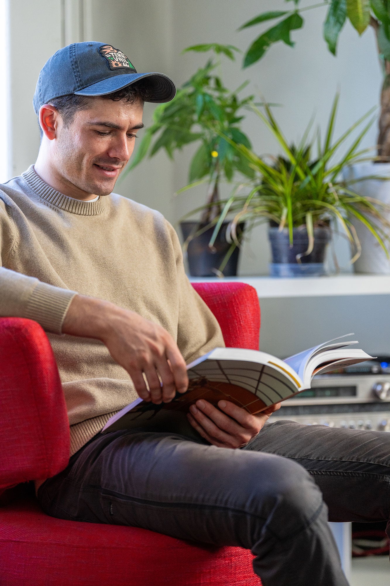 Man reading a book on a red chair in a room with plants