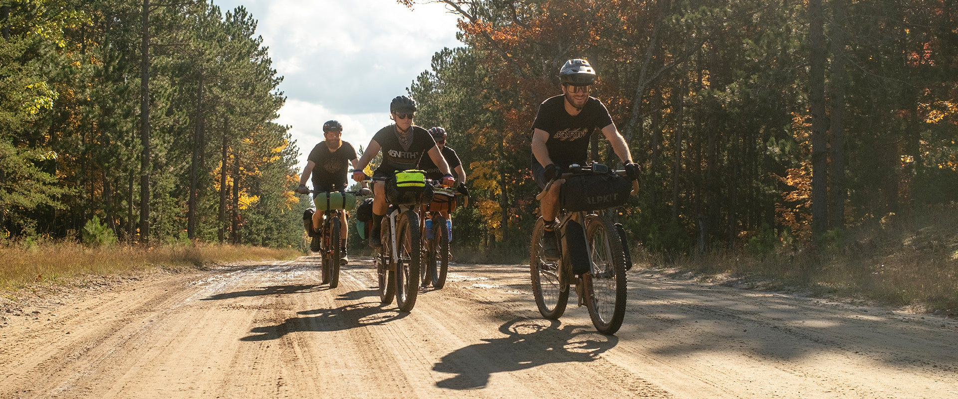 Four cyclists riding on forest gravel road together on loaded bikes for bikepacking