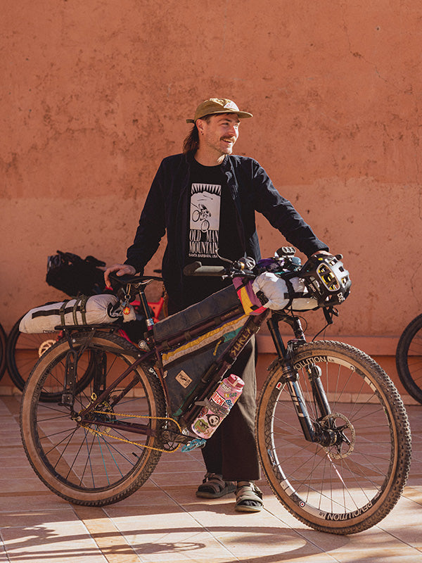 Eric House with a bicycle loaded with gear against a pink wall