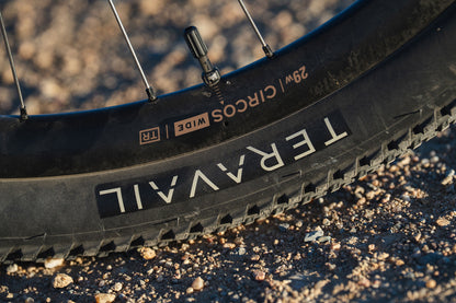 Close-up of a black bicycle tire with visible tread, valve stem, and sidewall branding reading TERAVAIL and CIRCOS WIDE, photographed outdoors on gravel.