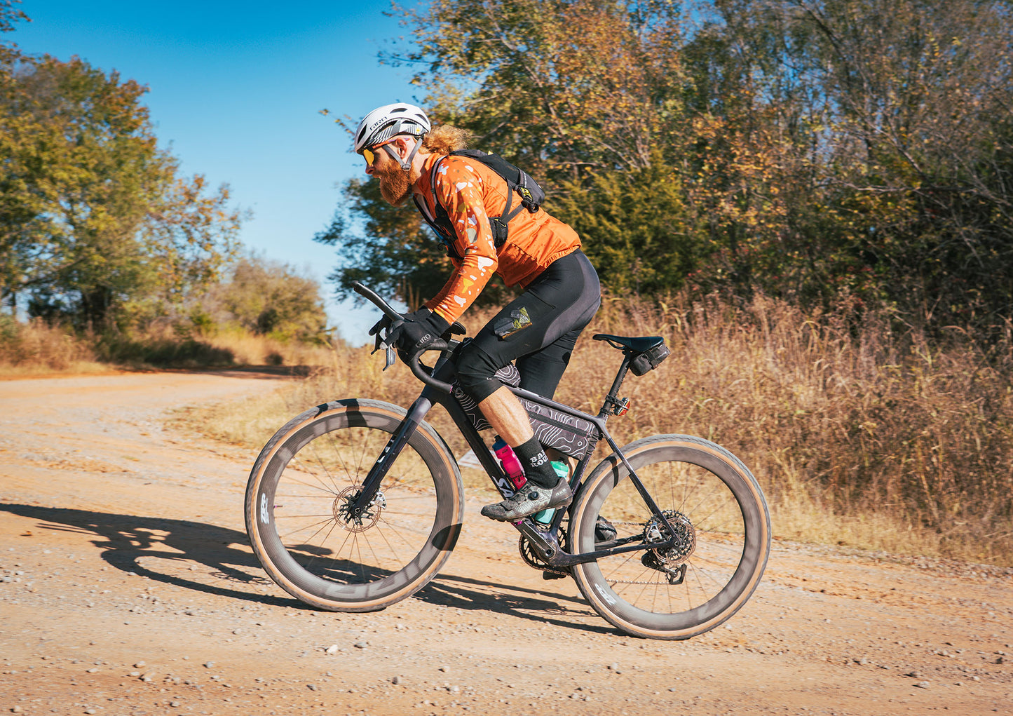 Person riding a bicycle on a dirt road with trees in the background