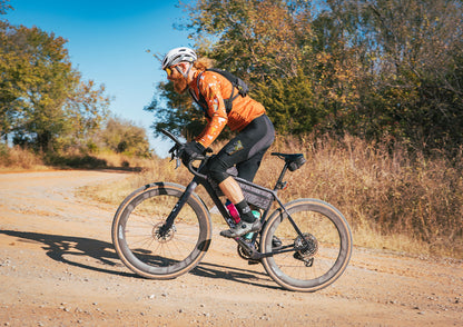 Person riding a bicycle on a dirt road with trees in the background
