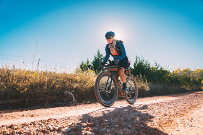 Person riding a bicycle on a dirt road with a clear blue sky