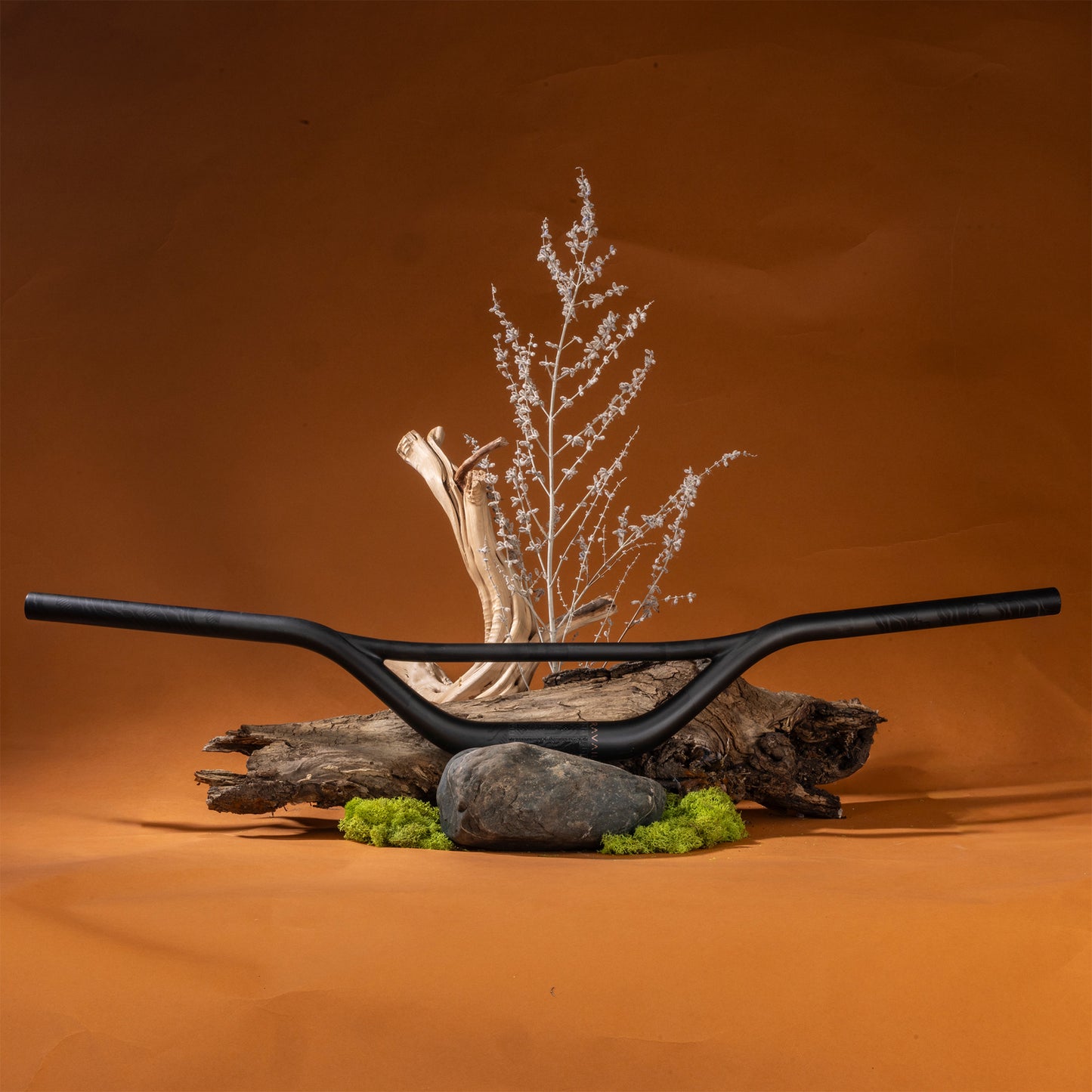 Decorative arrangement with Moonstone Carbon bar, glass sculpture, and rocks on a brown background