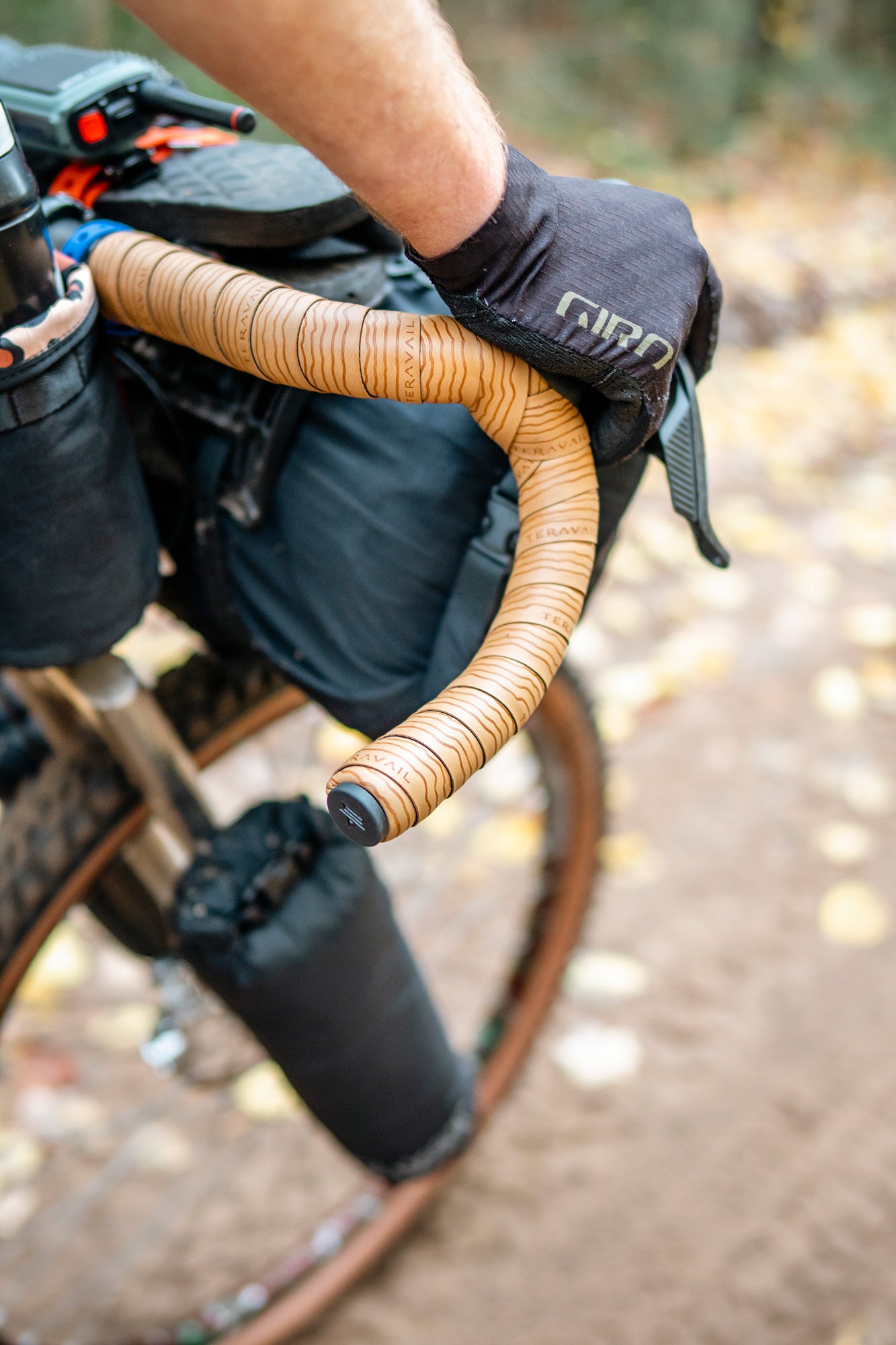 Close-up of a bicycle handlebar with a person wearing gloves, set against a blurred natural background.