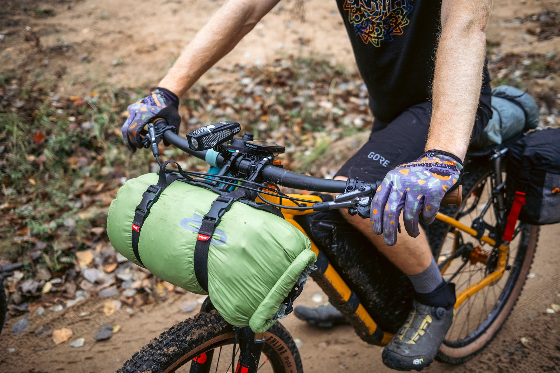 Person on a bicycle with gear attached, sitting on a dirt path.