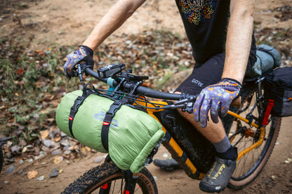 Person on a bicycle with gear attached, sitting on a dirt path.