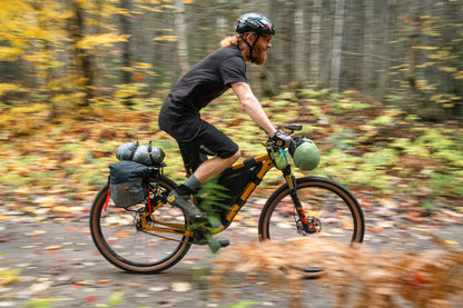 Person riding a bicycle with gear through a forest during autumn.