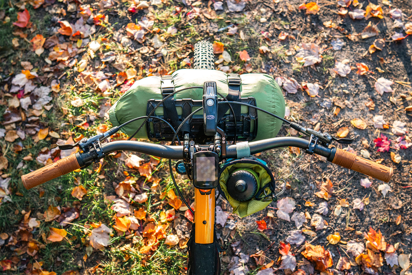 Bicycle handlebars with green bags on a ground covered with autumn leaves