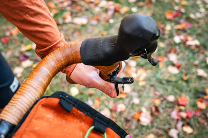 Close-up of a person holding a bicycle handlebar with autumn leaves in the background