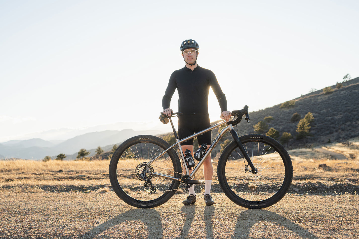 Man holding a bicycle in a desert landscape with mountains in the background