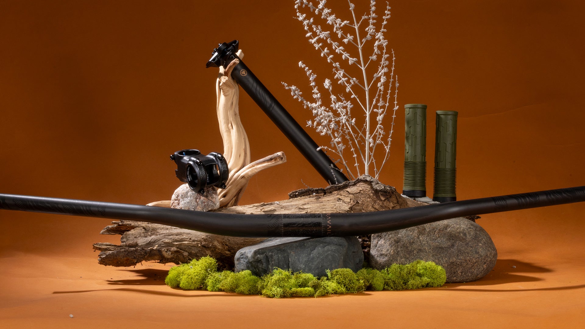 Decorative arrangement with a seatpost, stem, grips, handlebar, rocks, and plants on an orange background