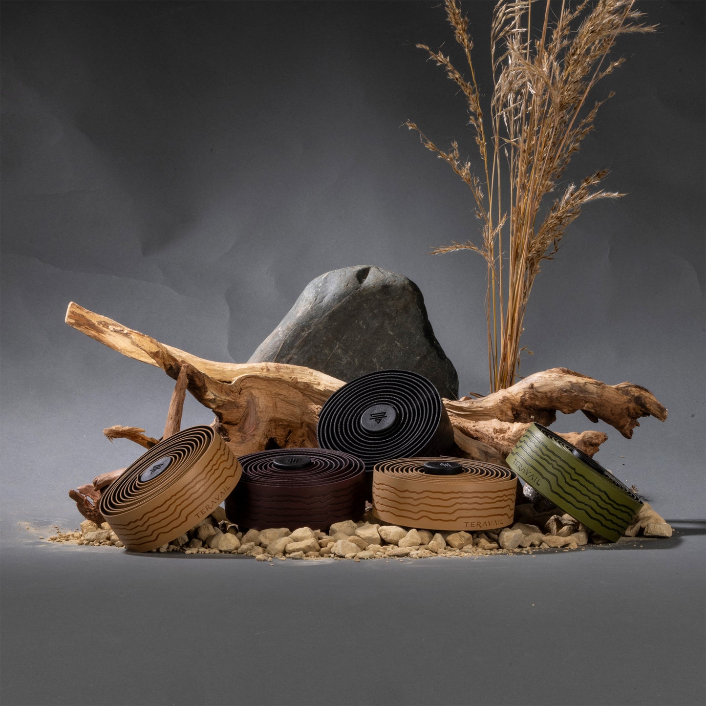 Rolls of Teravail colored bar tape set-up next to drift wood, rocks and brown plants on gray background