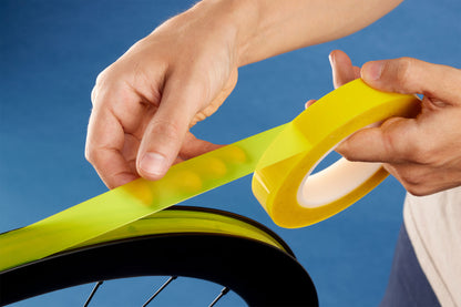 Person applying yellow tape to a bicycle rim against a blue background